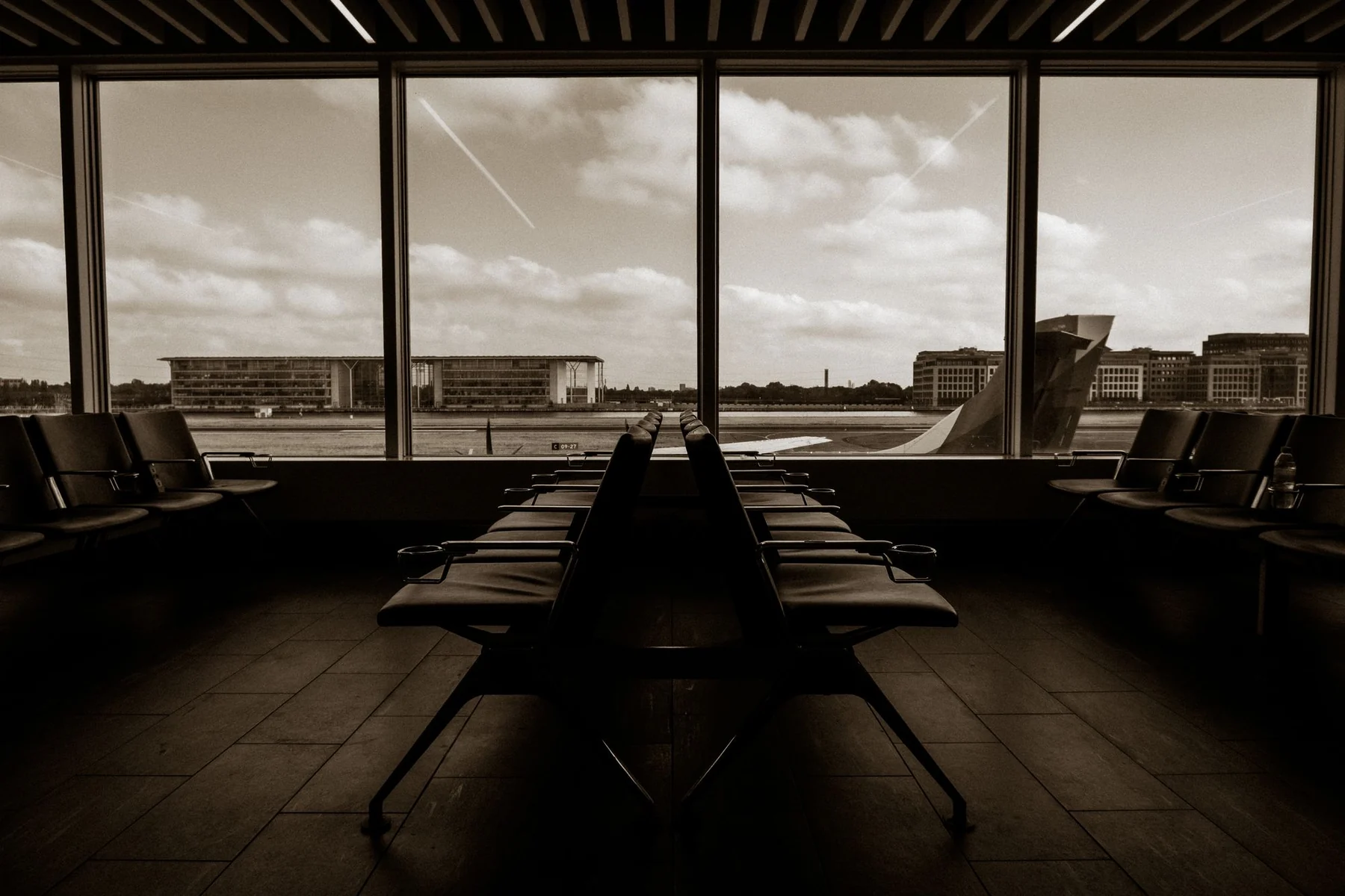 Quiet airport terminal in sepia tone overlooking runway and airplane wing.