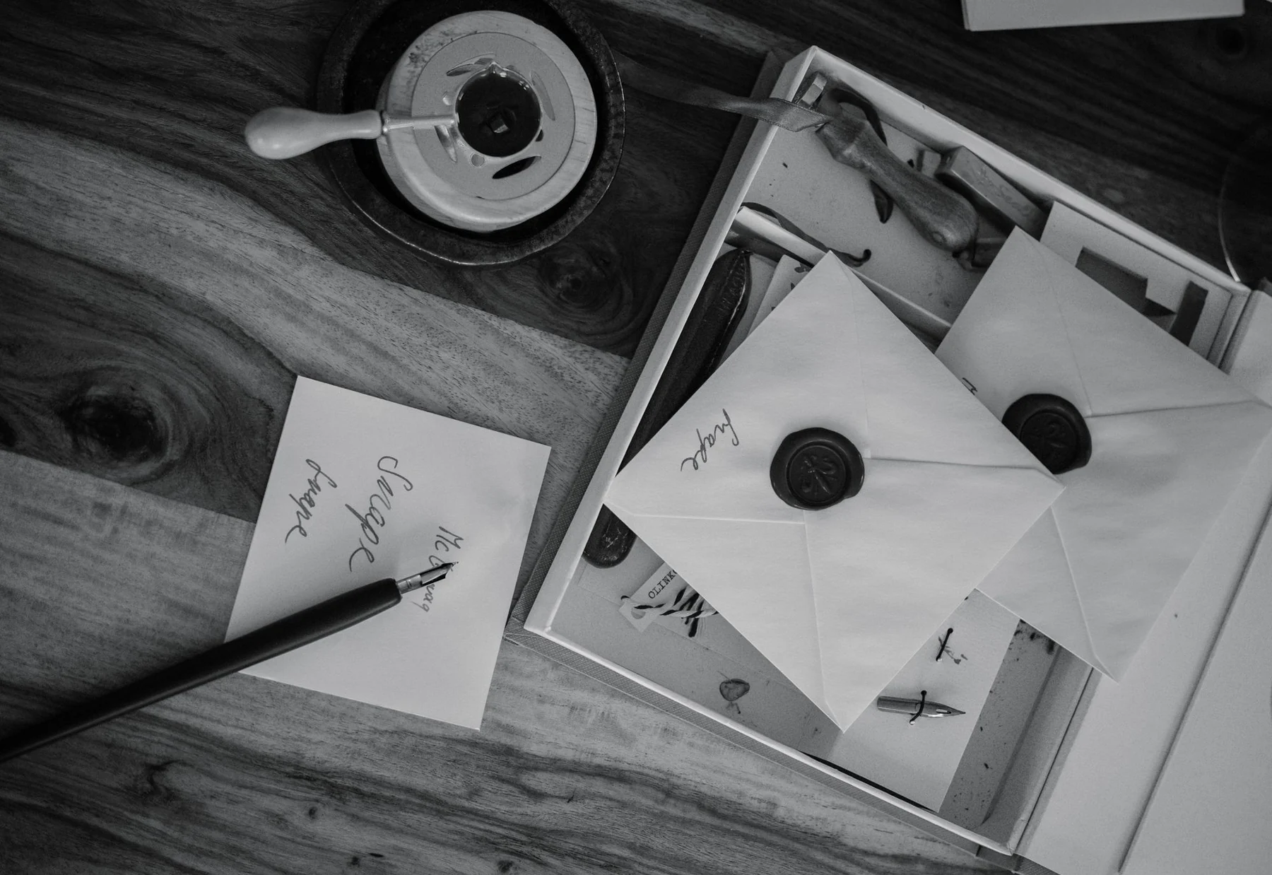 Black and white photo of vintage envelopes with wax seals and calligraphy tools on a wooden desk.