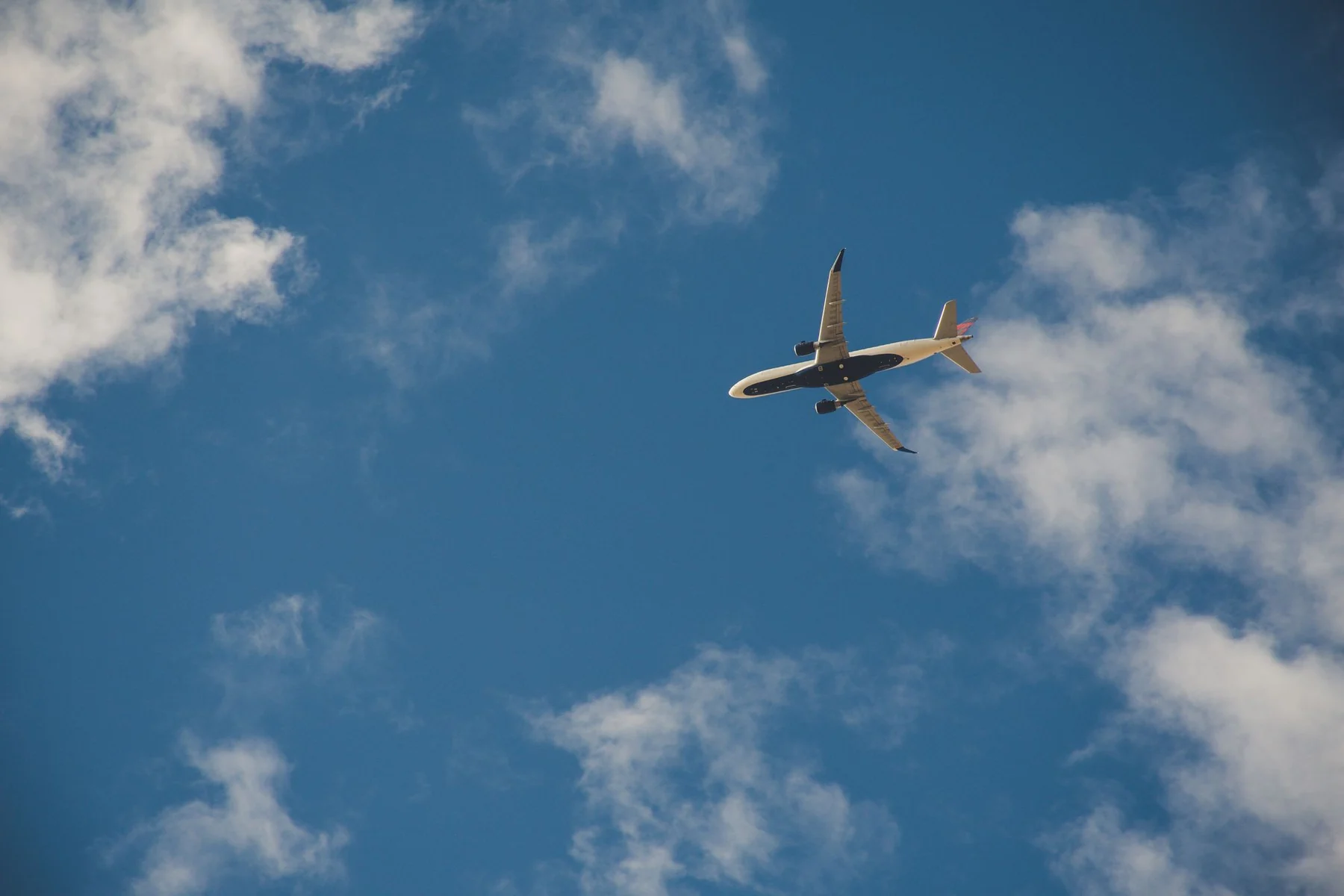 A commercial airplane flying high in the clear blue sky with clouds.