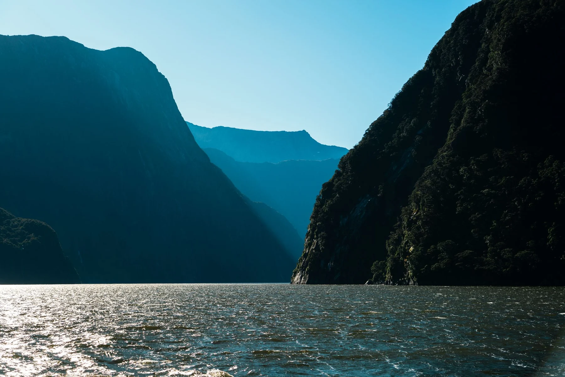 Tranquil view of Milford Sound's fjords and mountains under clear skies, New Zealand.