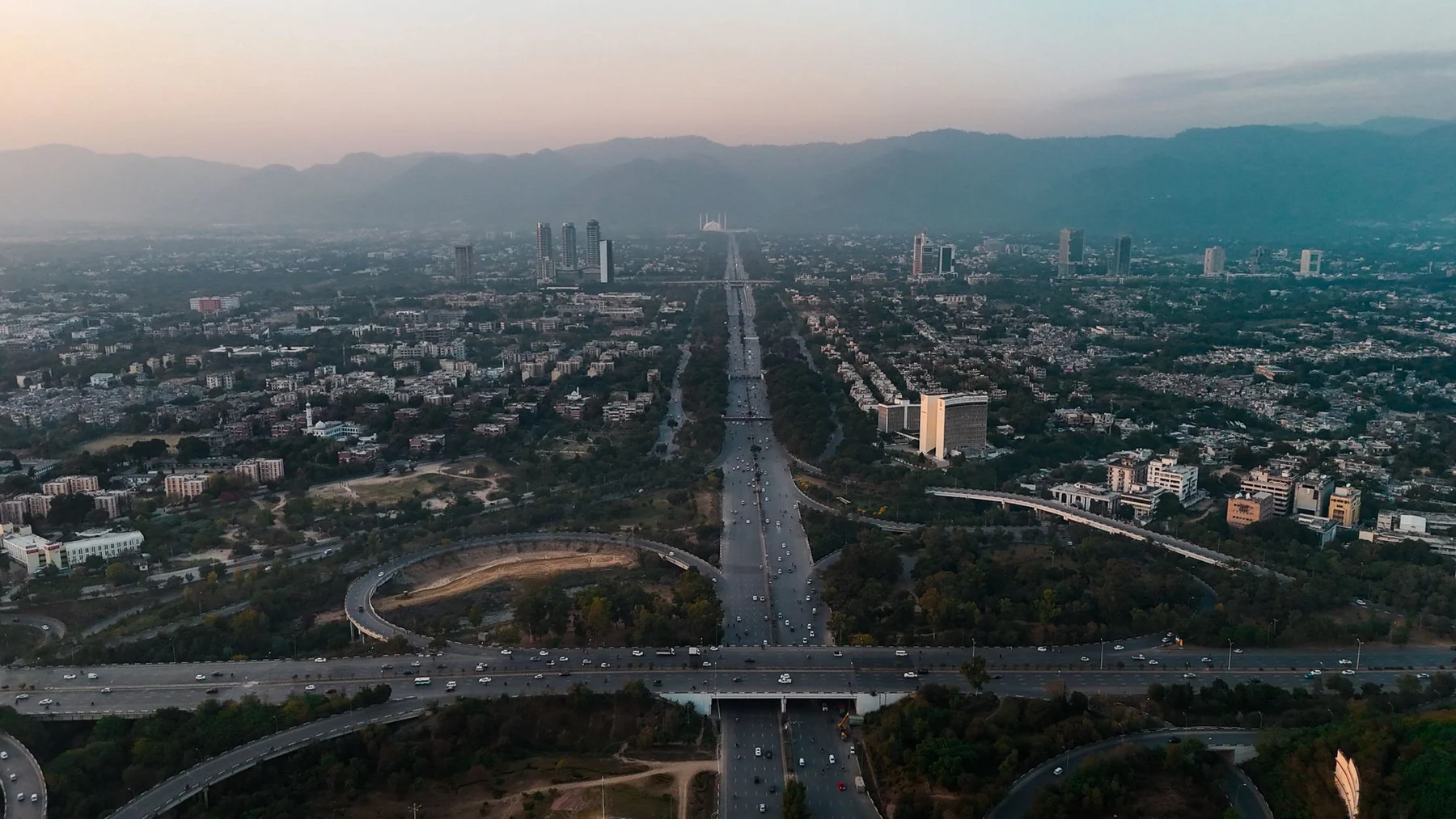 A stunning aerial view of Islamabad with highways, buildings, and mountains at dusk.