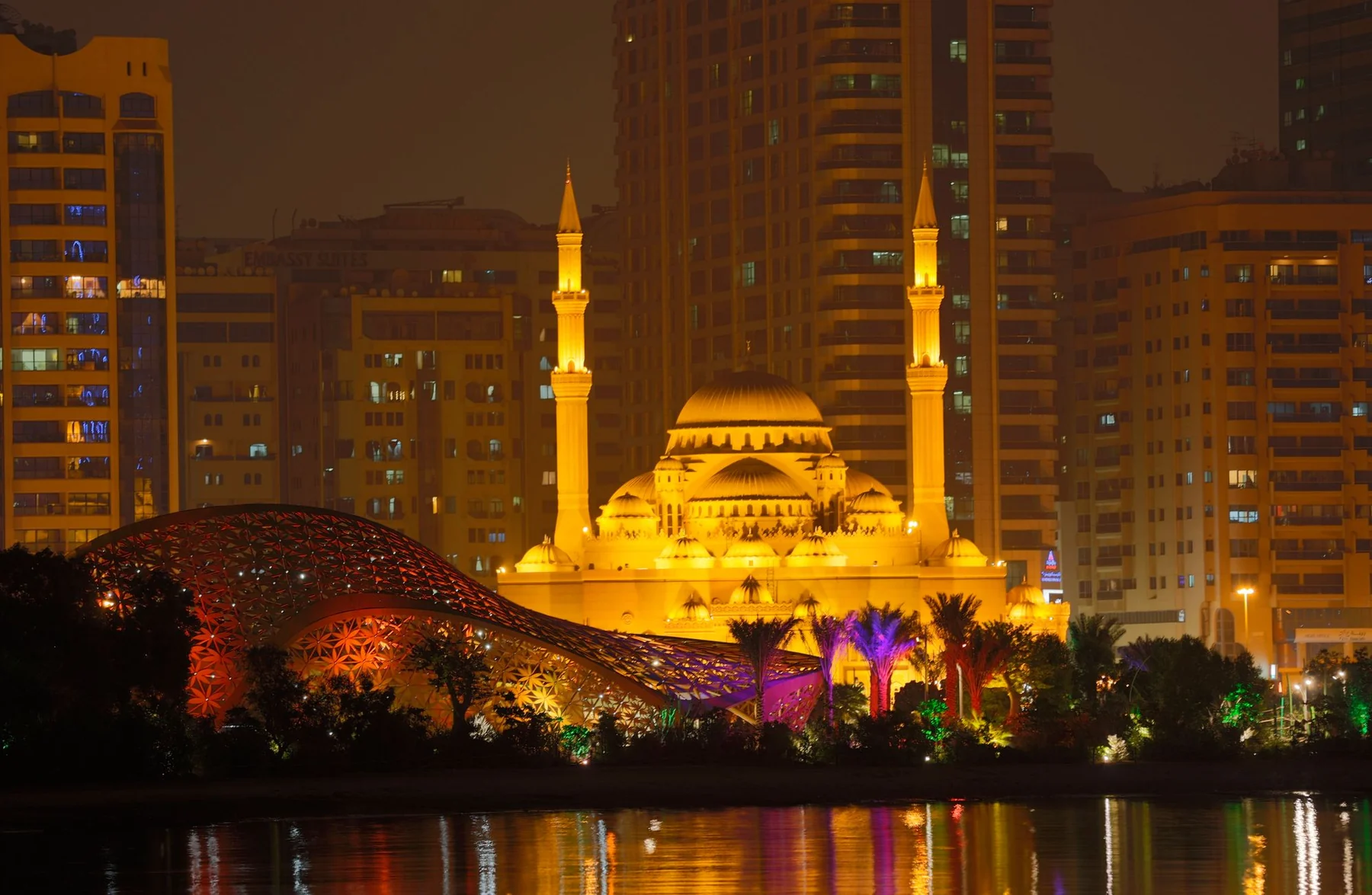 Stunning night view of the Al Noor Mosque with vibrant city backdrop in Sharjah, UAE.